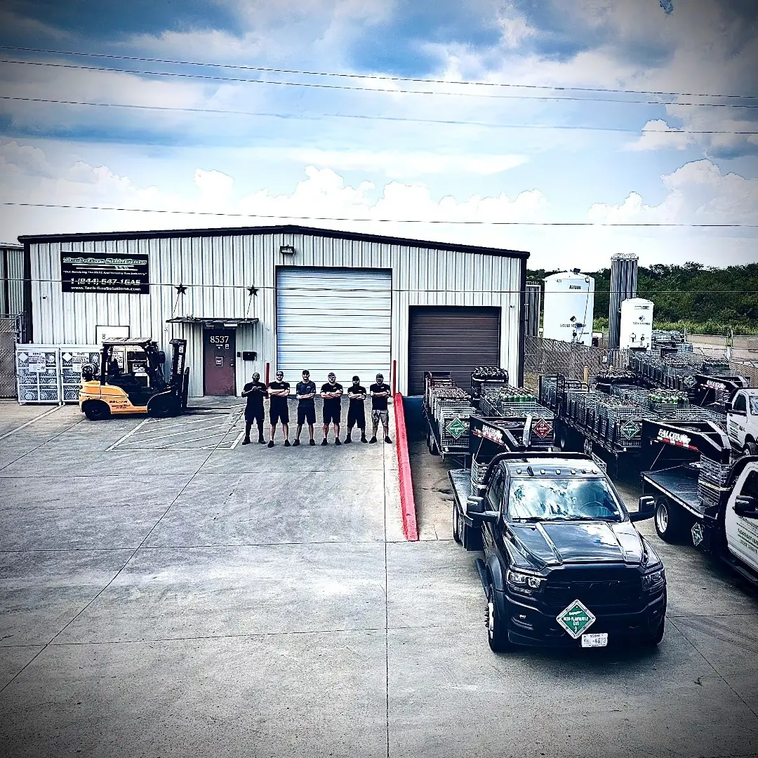 Tech Gas Solutions Dallas TX facility with staff lined up, cylinder trailers, forklifts, and delivery trucks ready for local and nationwide shipments.