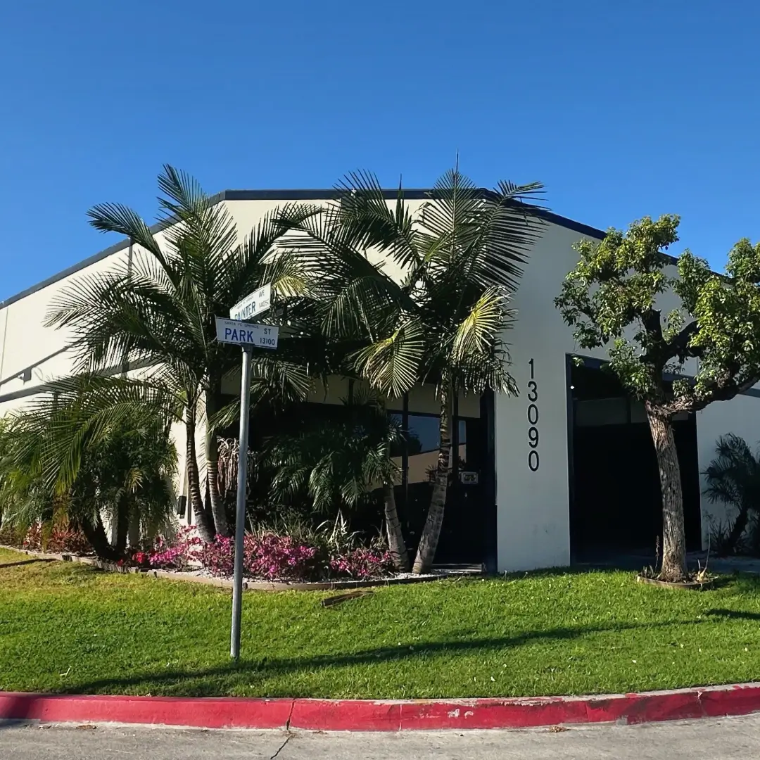 White commercial building with lush palm trees in front, blue sky above, and a red-curb lawn edge preparing the entrance.